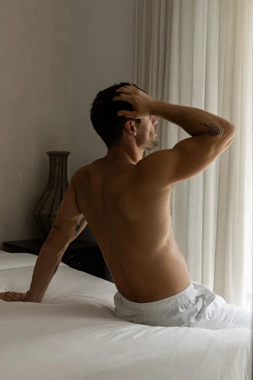 Homme assis sur un lit, au réveil, dans une lumière douce du matin