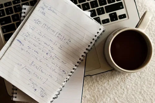 Carnet ouvert avec des notes manuscrites posé sur un ordinateur, tasse de café à côté, symbole d’écriture intuitive et de transmission médiumnique